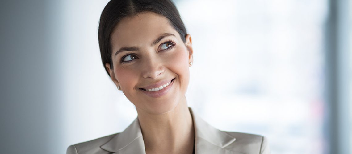 Closeup portrait of smiling beautiful middle-aged business woman wearing jacket and looking up at copy space with her head tilted. Front view.